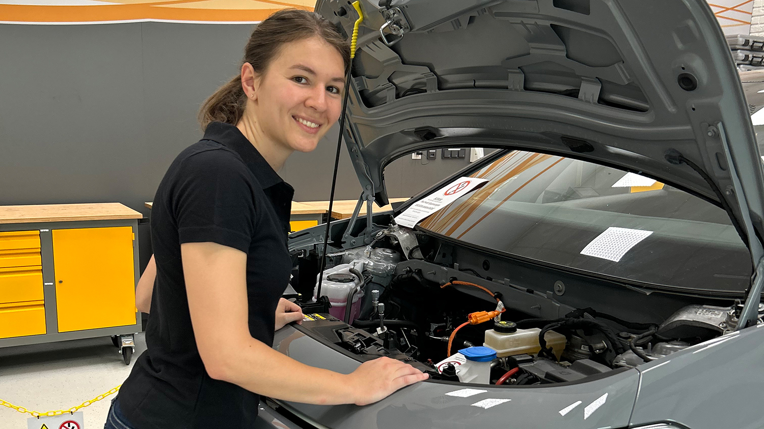 Continental Mitarbeiterin steht vor offener Motorhaube eines grauen Pkw.